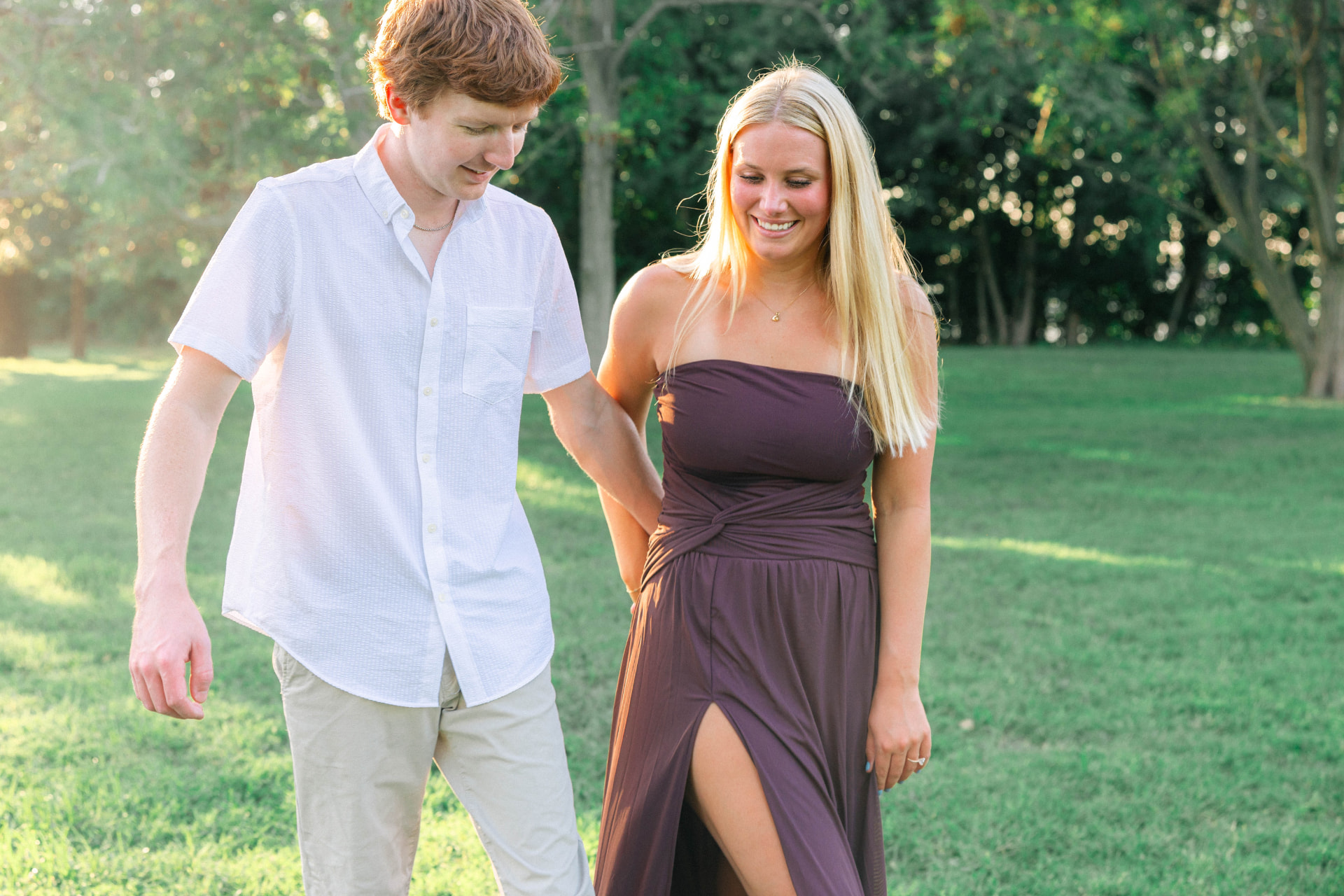 Colin and Samantha walking arm in arm through the park at golden hour