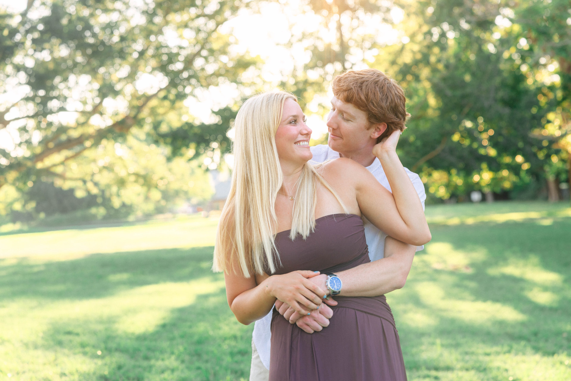Colin holding Samantha from behind in a sunlit park