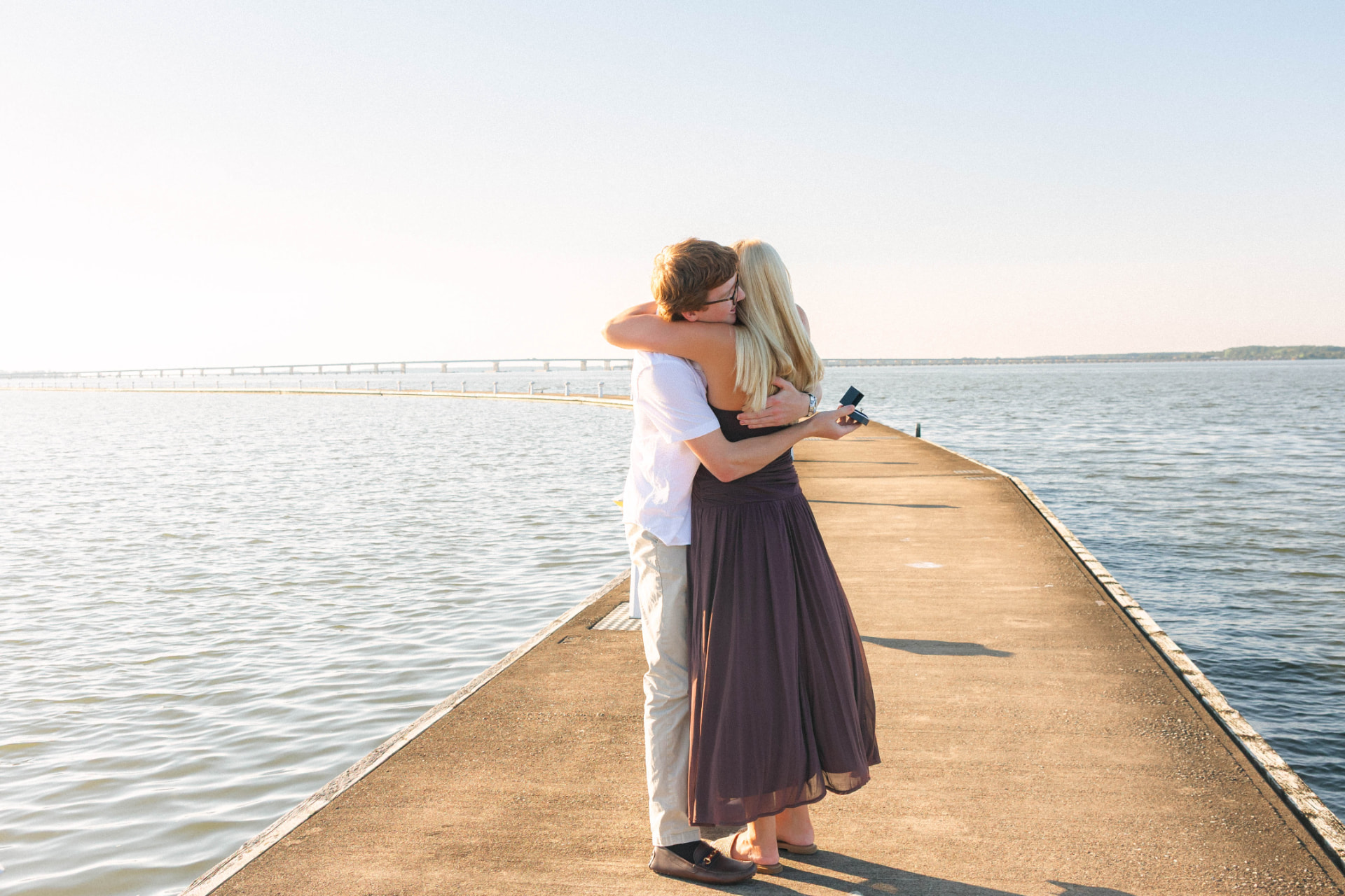 Samantha and Colin hugging on the pier, Colin holding the ring box behind her